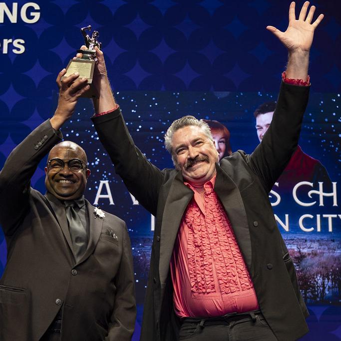 Anvil Award winner on stage holding trophy in the air with a host