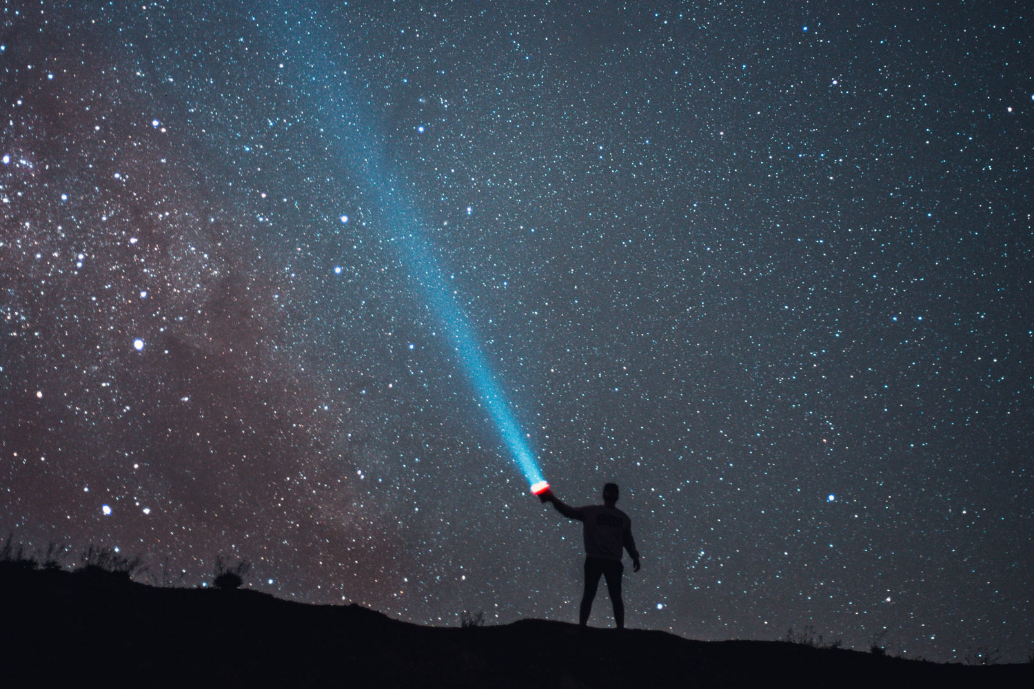 man shining flashlight into dark sky