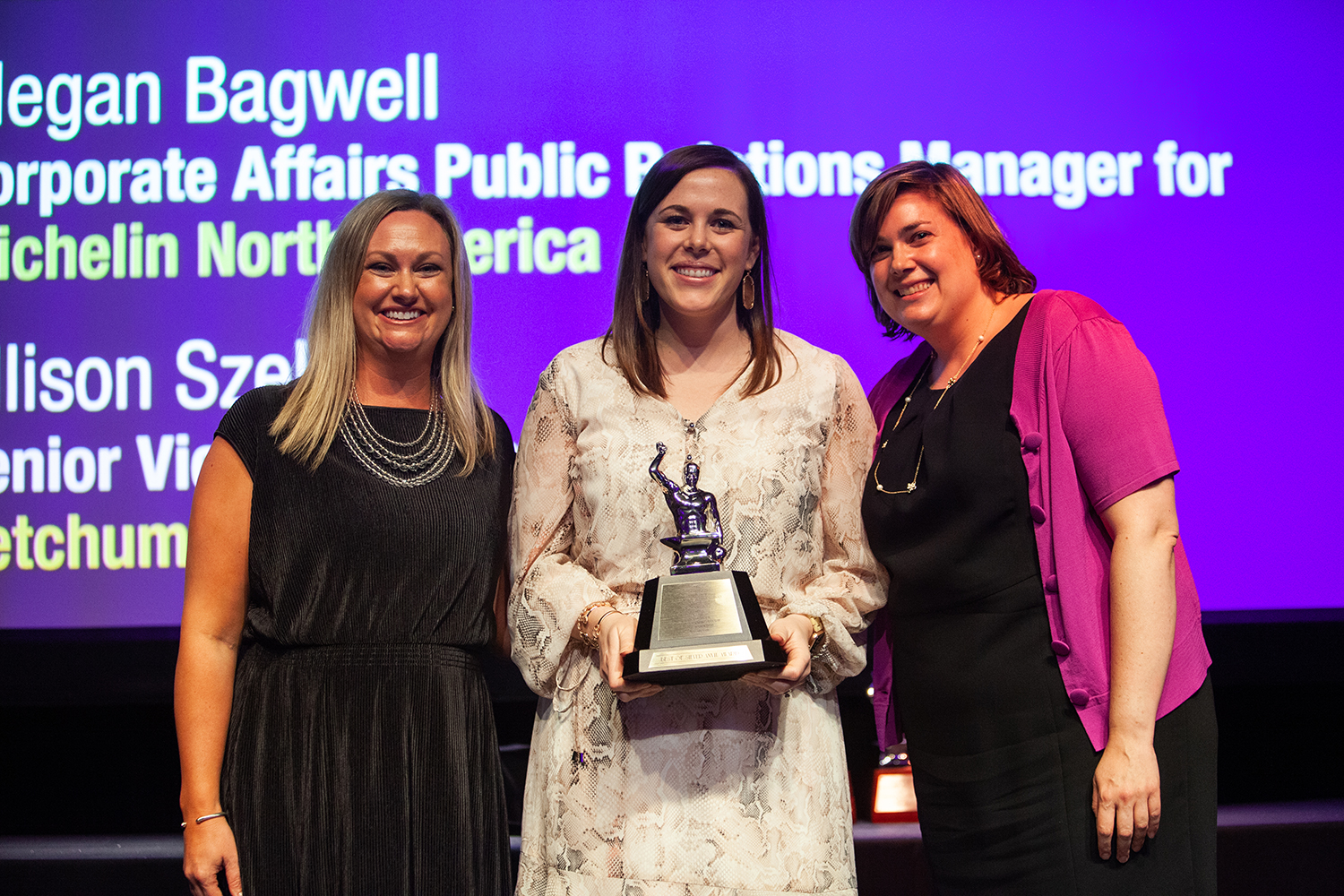 Michelin standing in-between two people, holding her Silver Anvil trophy at the International Conference