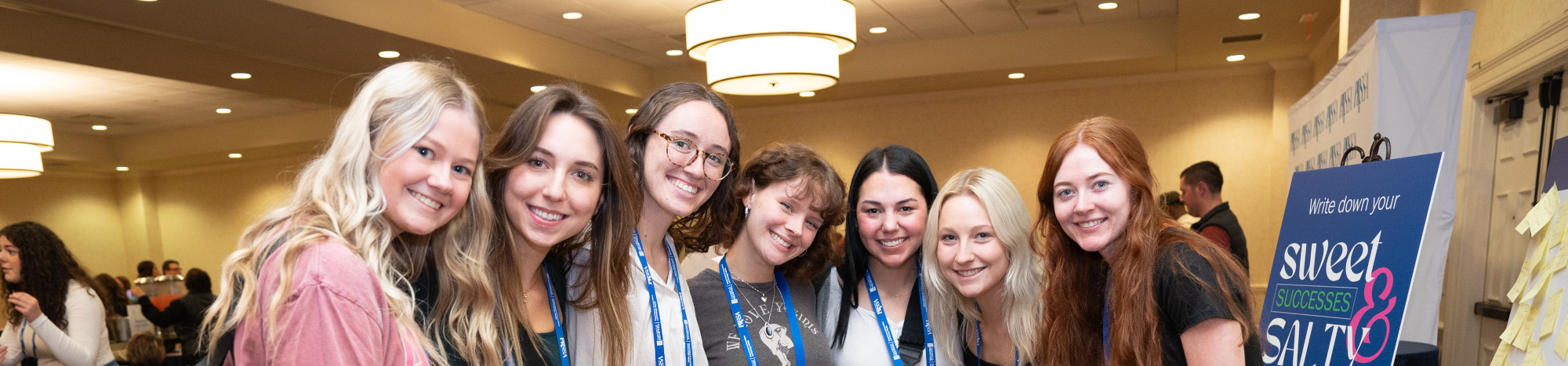 Seven PRSSA students in front of logo backdrop