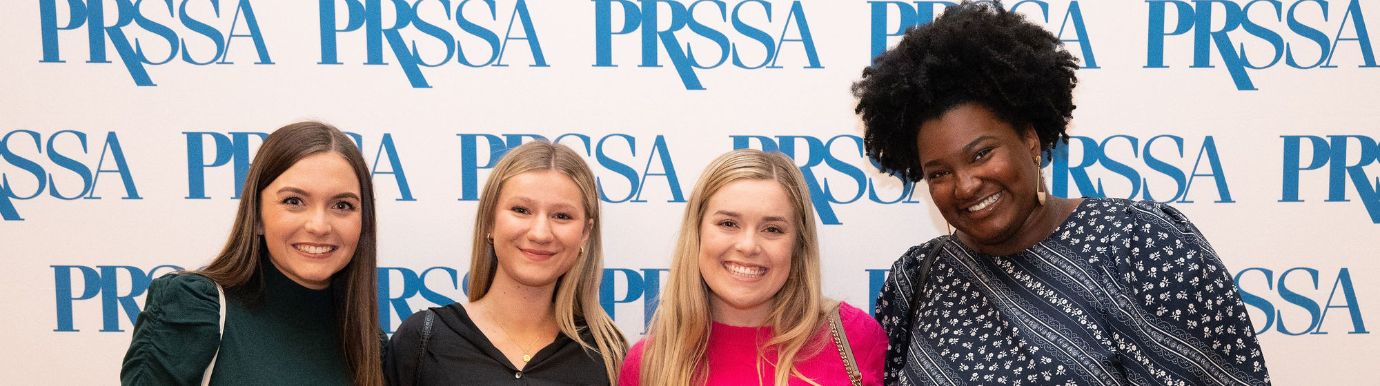 Seven PRSSA students in front of logo backdrop