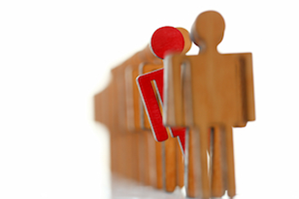 Wooden people stacked on in front of the other with a red person sticking out to represent uniqueness. Photo Source: [shutterstock]